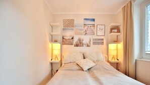 Un dormitorio con una cama, dos lámparas de noche y una serie de cuadros enmarcados en la pared.