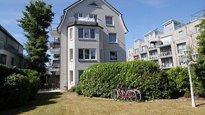 A multi-story residential building with balconies, a well-maintained lawn, and bicycles parked outside.