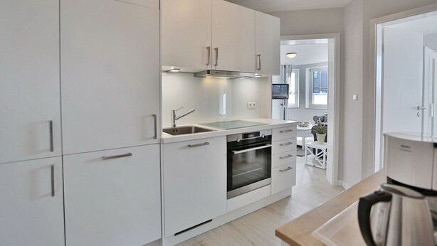 A modern kitchen with white cabinetry, stainless steel appliances, and a wooden countertop.