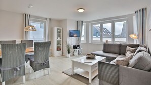 A modern living room with a sofa, dining table, chairs, a TV, and a bookshelf.