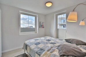 Una camera da letto con un letto, due finestre, un quadro e una lampada.