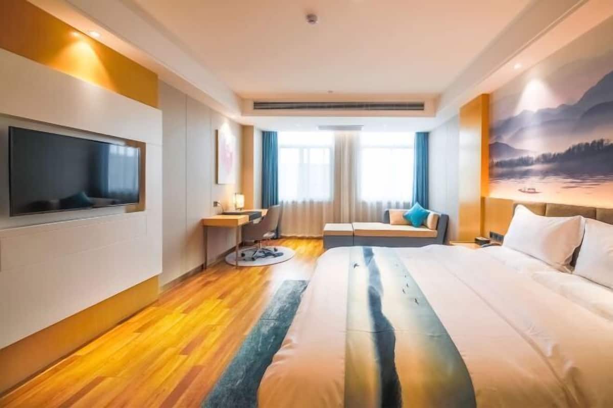 A hotel room with a bed, a desk, a TV, and a large window.