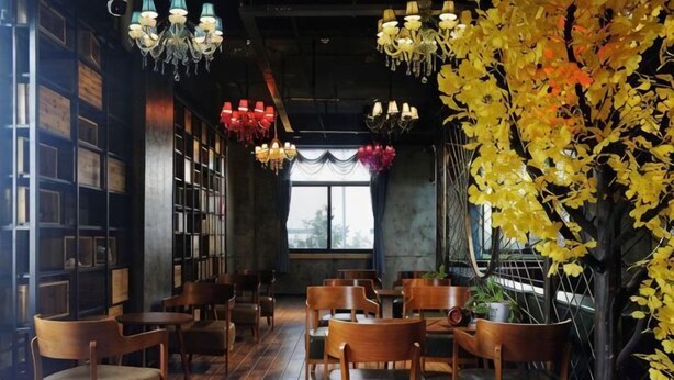 A cozy restaurant with wooden tables and chairs, hanging lights, and a large window with a view.