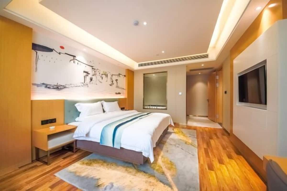 A modern hotel room with a bed, bedside table, artwork on the wall, and a television.
