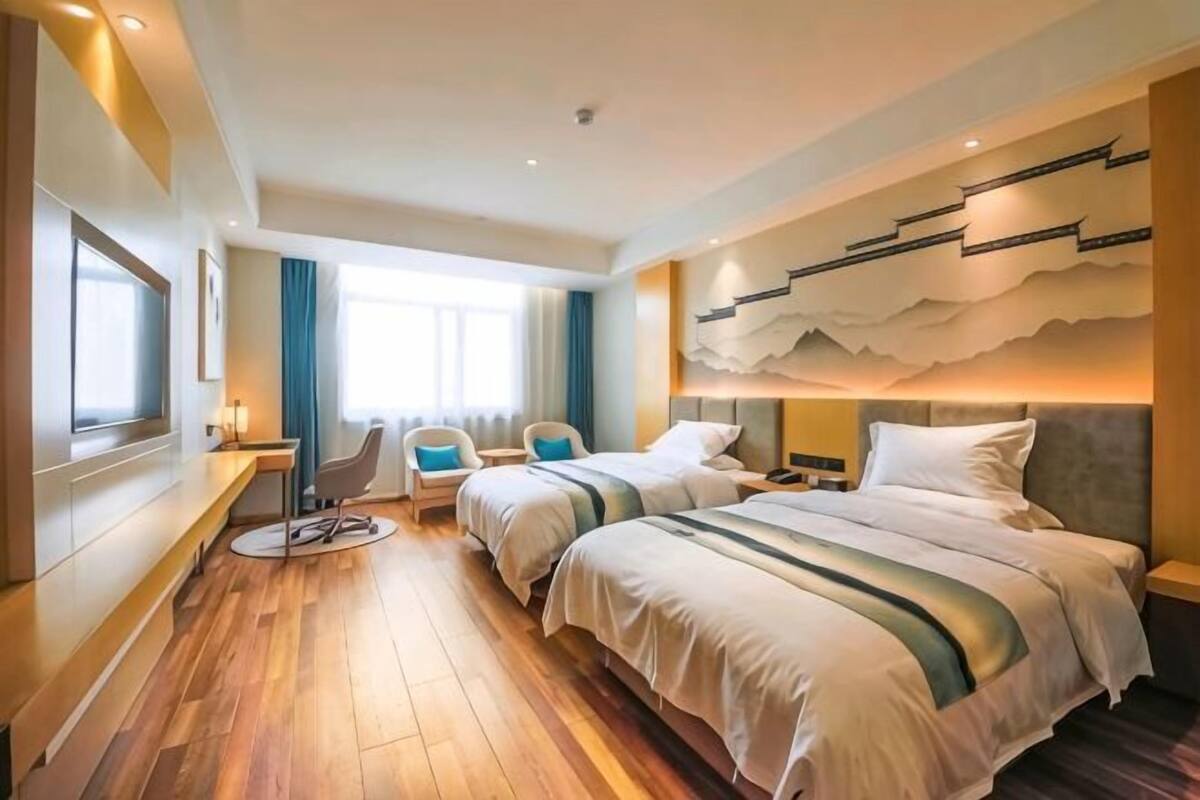 A hotel room with two beds, a desk, a chair, and a large window.