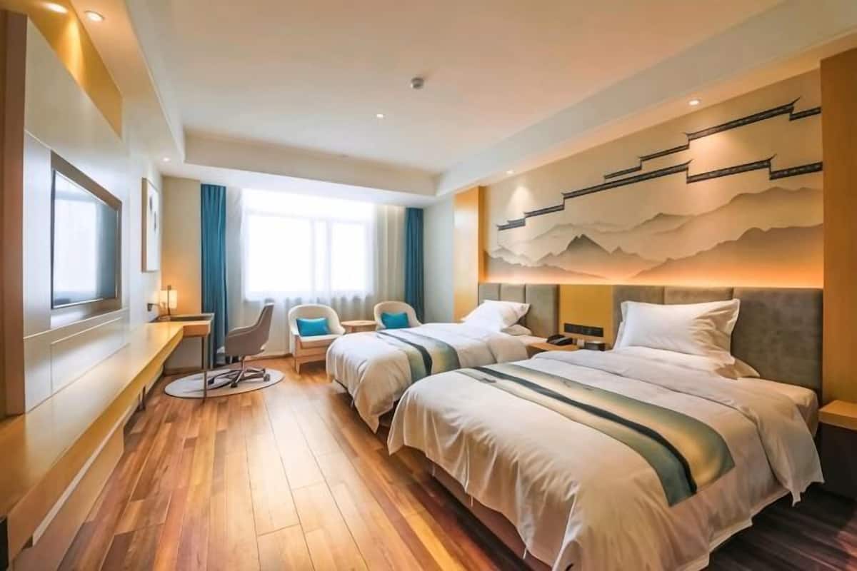 A hotel room with two beds, a desk, a chair, and a large window.