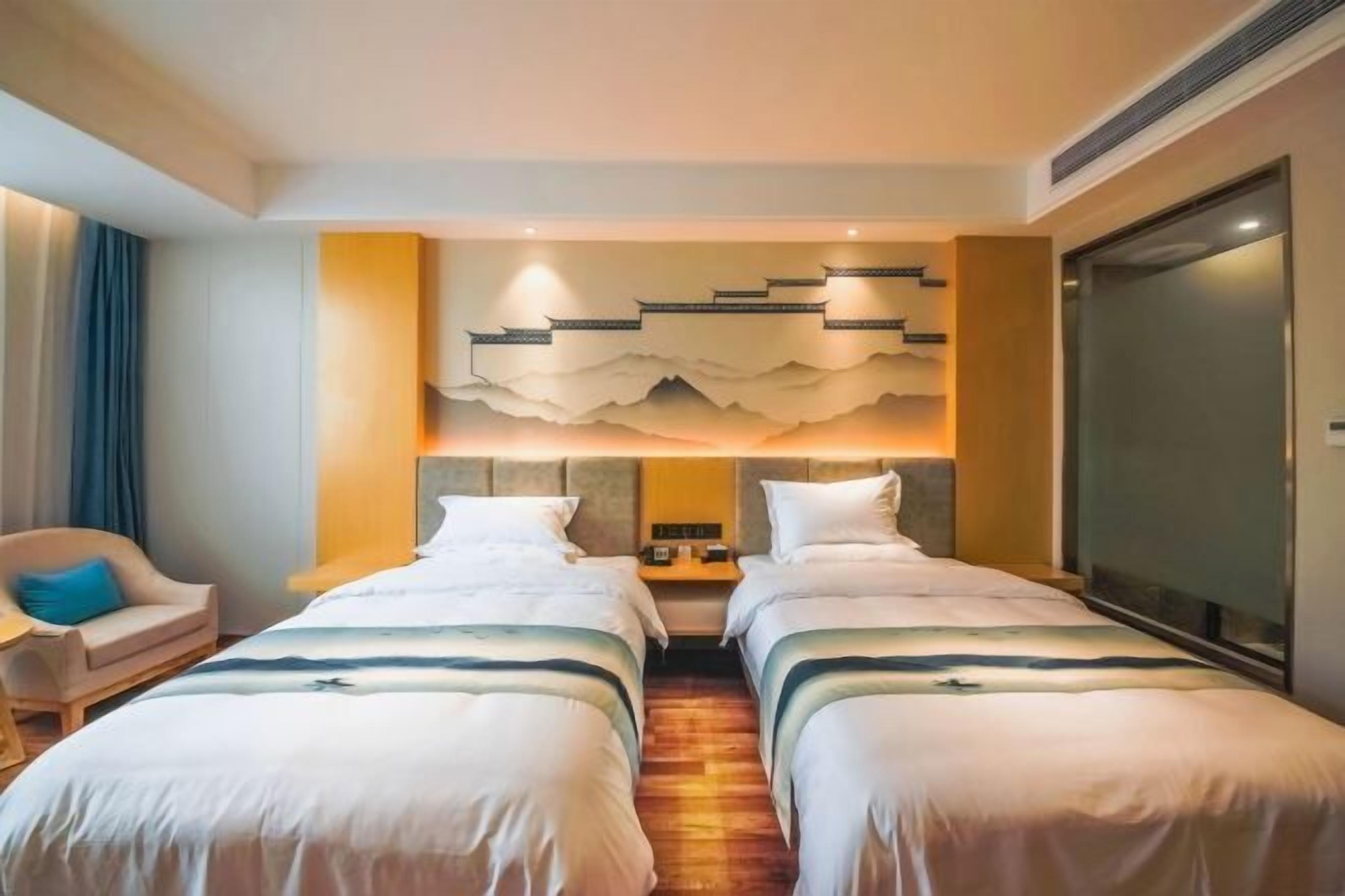 Habitación de hotel con dos camas, una silla, un adorno en la pared y un ventanal grande.
