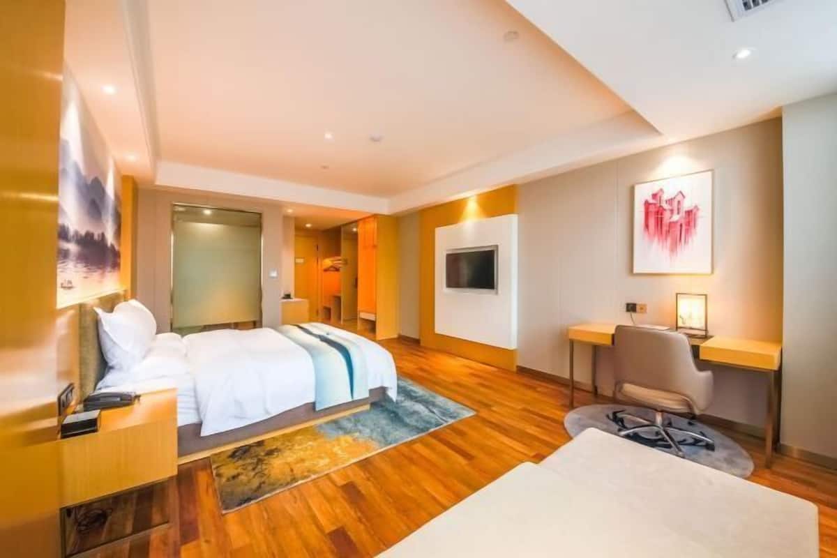 A modern hotel room with a bed, desk, chair, TV, and artwork.