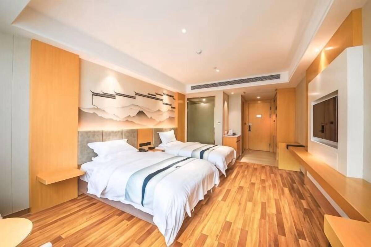 A hotel room with two beds, a TV, and a wooden floor.