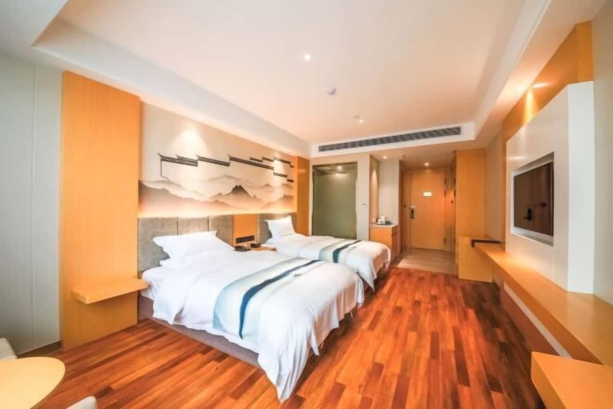 A hotel room with two beds, a wooden floor, a wall-mounted TV, and a modern design.