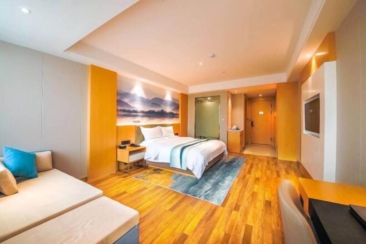A hotel room with a bed, a sofa, a desk, and a painting on the wall.