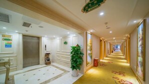 A hotel corridor with a marble floor, a potted plant, a reception desk, and a sign indicating the direction to the elevator. - Vienna Hotel (Jishou Qianzhou Ancient City Branch) (Jishou)