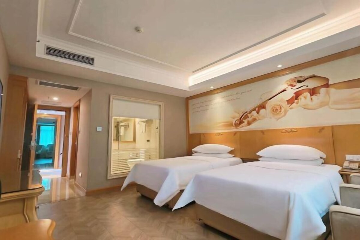 A hotel room with two beds, a large mirror, a wall-mounted artwork, and a wooden headboard.