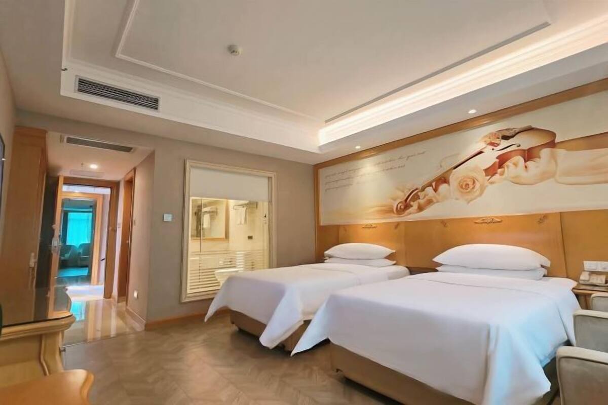 A hotel room with two beds, a wooden headboard, a large wall mural, and a view of the hallway.