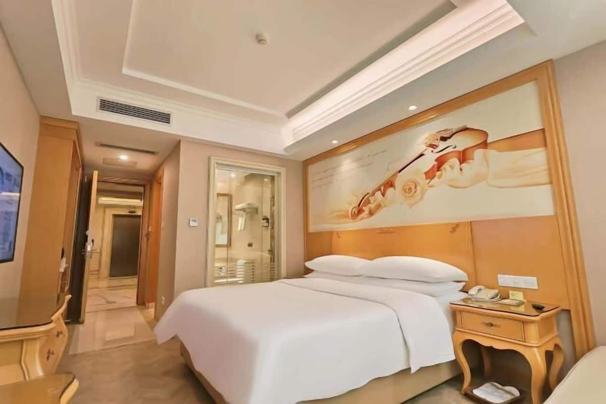A hotel room with a large bed, a bedside table with a phone, and a painting on the wall.