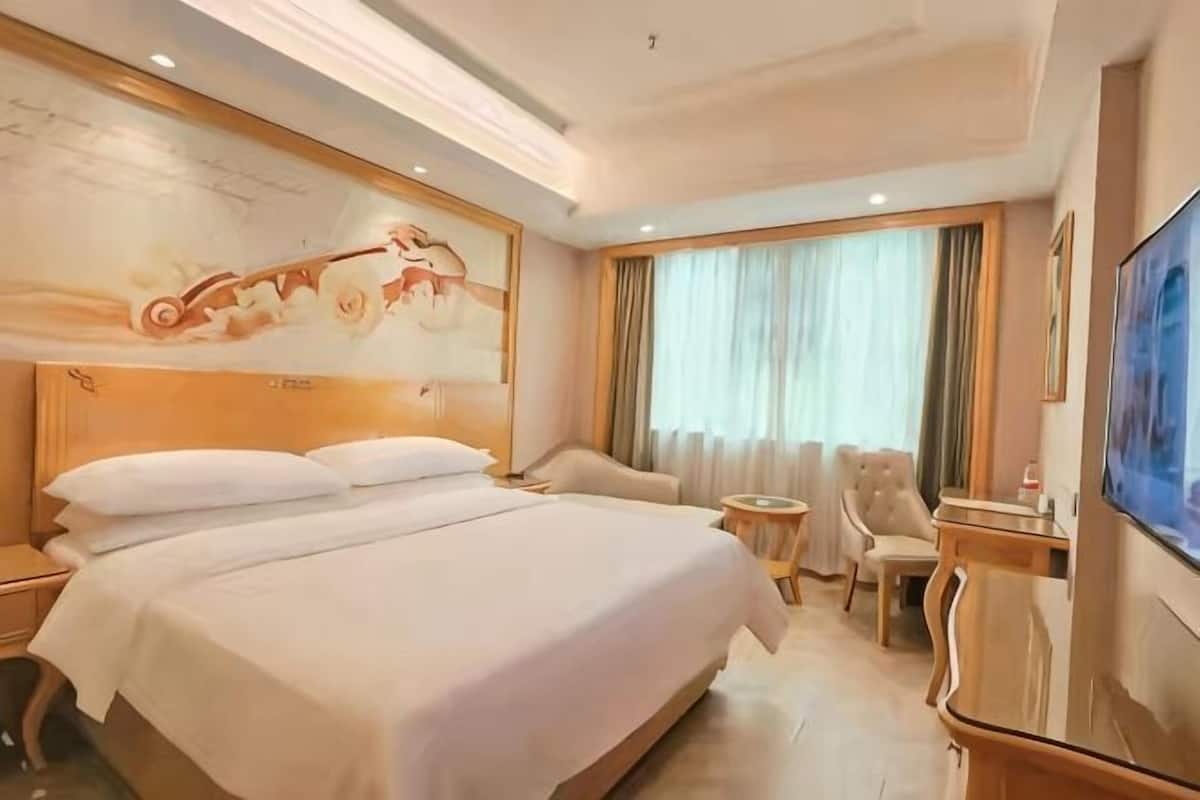 A hotel room with a large bed, a desk, a chair, and a television.