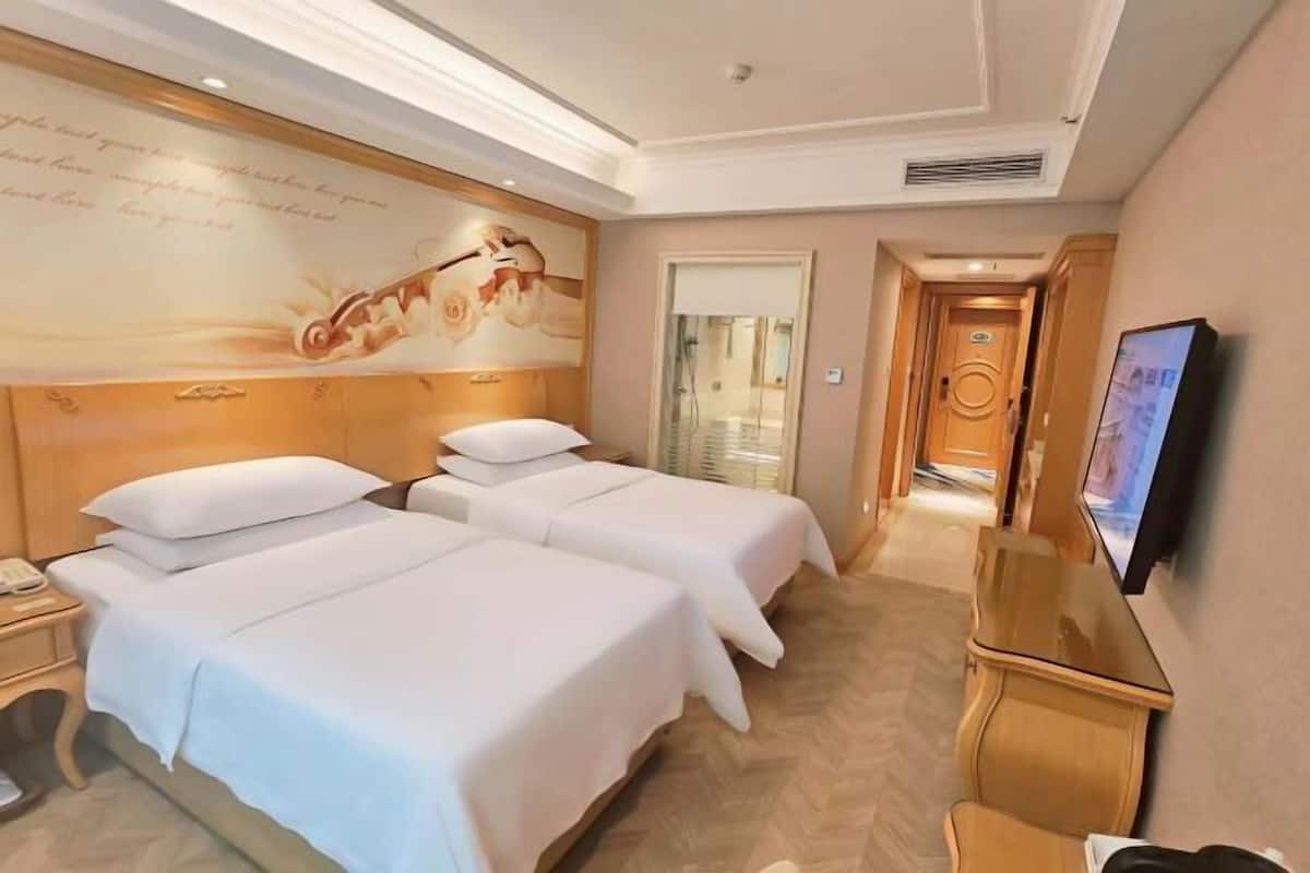 A hotel room with two beds, a television, a wooden headboard, and a large wall mural.