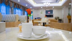 A dining area with a table set for two, featuring a white tablecloth, a white bowl, a white cup, and a glass of water. A red rose is placed in a vase on the table. - Vienna Hotel (Jishou Qianzhou Ancient City Branch) (Jishou)