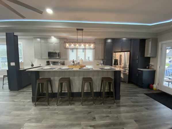 Una cocina moderna con una isla central, taburetes de bar, electrodomésticos de acero inoxidable y una lámpara colgante.