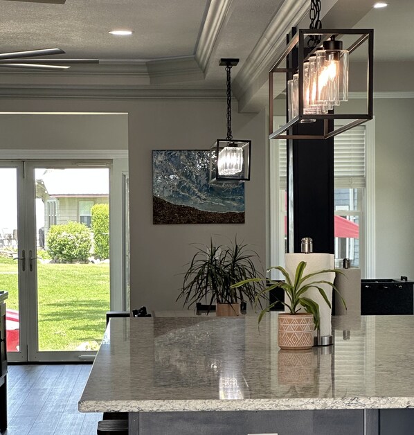 A modern kitchen with a marble countertop, pendant lights, and a large painting on the wall.