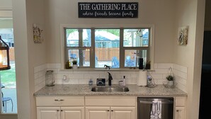 A kitchen with white cabinets, a stainless steel dishwasher, and a window with a view of the backyard. - Charming new home near Canyon Lake/Guadalupe River (Canyon Lake)