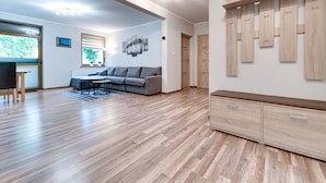 A spacious living room with a wooden floor, a grey sofa, a dining table, and a wall-mounted wooden cabinet with hooks. - Karpacz Boczna by Interhome (Karpacz)