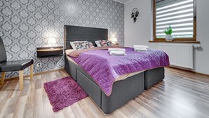 A modern bedroom with a large bed, a nightstand, a chair, and a window with blinds. - Karpacz Boczna by Interhome (Karpacz)