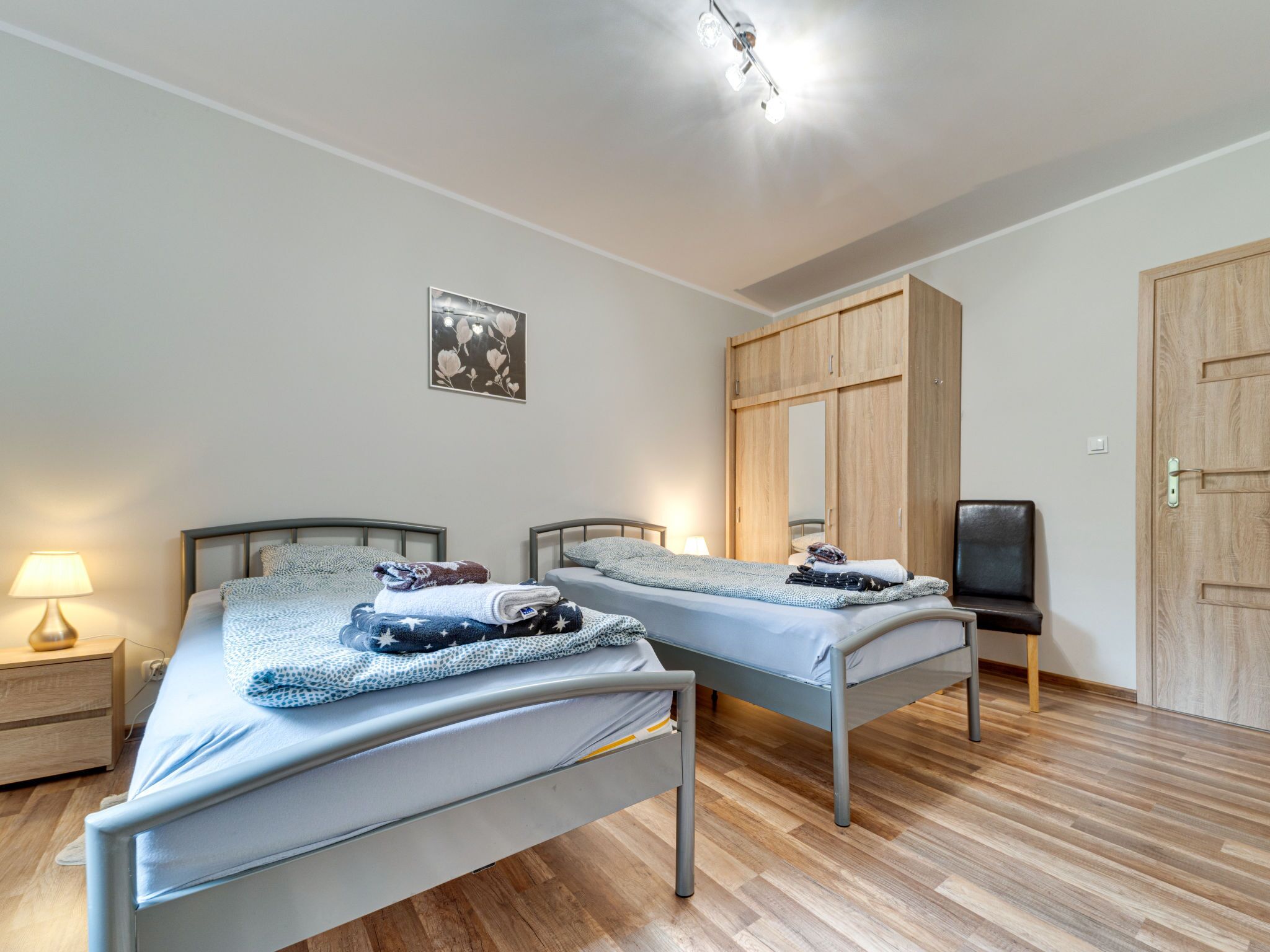 Une chambre avec deux lits simples, une armoire en bois, une télévision et une table de chevet avec une lampe.