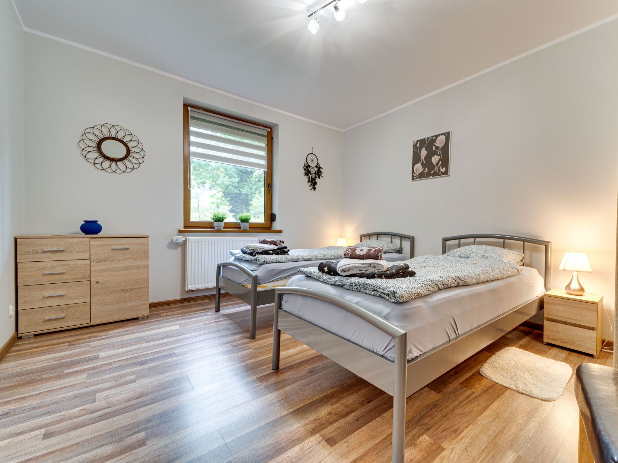 Un dormitorio con dos camas individuales, un aparador de madera, una ventana con persianas y un reloj de pared.