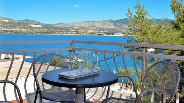 Ein Balkon mit Tisch und Stühlen mit Blick auf ein Gewässer und sanfte Hügel in der Ferne.