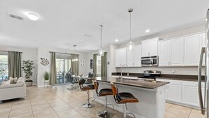 Una cocina moderna con gabinetes blancos, un refrigerador de acero inoxidable, un microondas y una barra con taburetes.