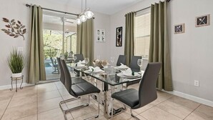 Un comedor con una mesa de vidrio, sillas negras y cortinas verdes.
