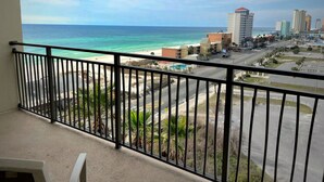 A balcony with a view of a beach, a parking lot, and a cityscape with buildings.