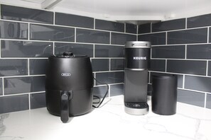 A kitchen with black tiled backsplash, a coffee maker, a kettle, and a thermos.