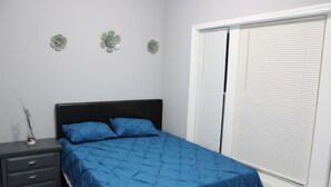 Een slaapkamer met een bed, een nachtkastje en een raam met jaloezieën.