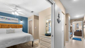 A bedroom with a bed, a dresser, a ceiling fan, and a painting on the wall.