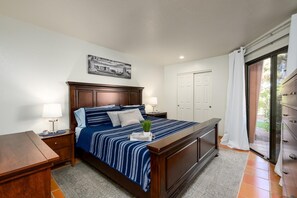 A bedroom with a large bed, two bedside tables, a nightstand, a window with curtains, and a door.