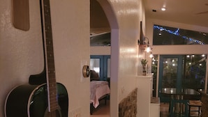 Ett rum med en gitarr, en säng, en matplats med ett bord och stolar samt en utsikt genom ett fönster.