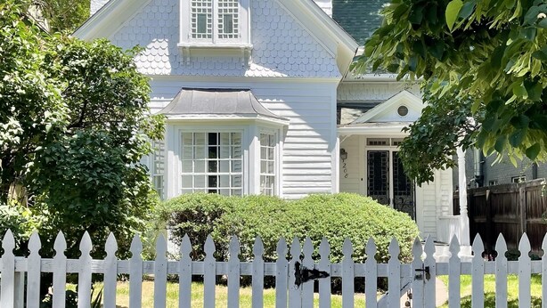 A white two-story house with a gabled roof, a front porch, and a white picket fence. - "The Cottage" Downtown Denver (Denver)