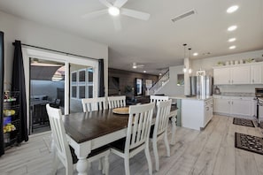 A spacious kitchen with white cabinetry, a dining area with a dark wooden table and white chairs, and a ceiling fan.
