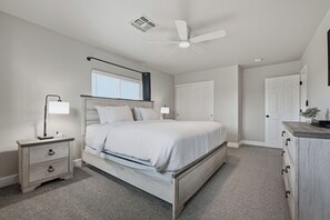 Quarto com cama, mesas de cabeceira, ventilador de teto, janela e porta.