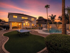 A two-story house with a swimming pool, outdoor seating, and a well-maintained lawn.