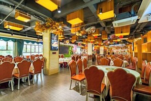 A restaurant with multiple tables and chairs, a large pillar with decorations, and a view of the outdoors. - City Encounter Boutique Art Hotel (Zhuhai)
