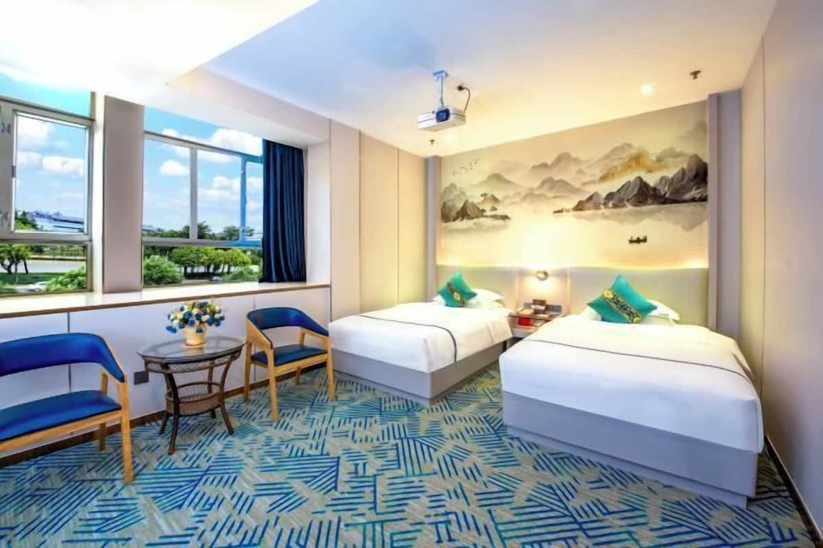 Ein Hotelzimmer mit zwei Betten, einem Schreibtisch mit Stuhl, einem kleinen Tisch mit Vase und einem Wandbild.