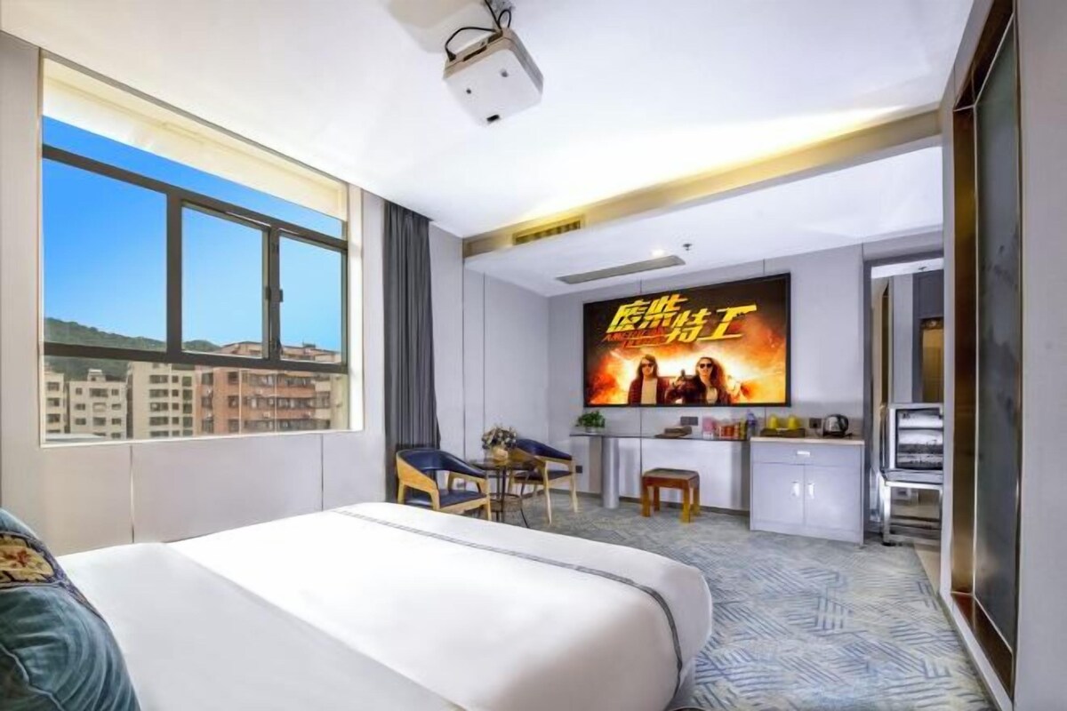 A hotel room with a large bed, a desk, a TV, and a view of the city.