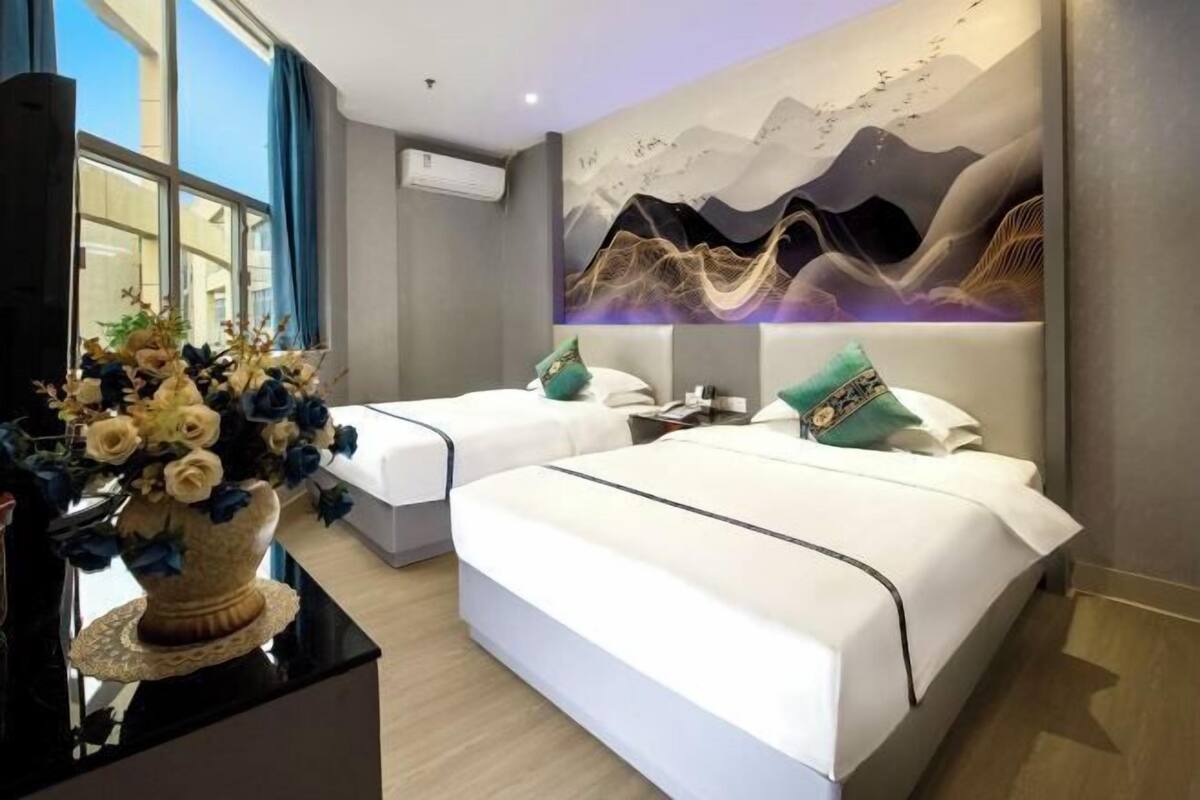 Ein Hotelzimmer mit zwei Betten, einem großen Fenster und einem Wandgemälde.