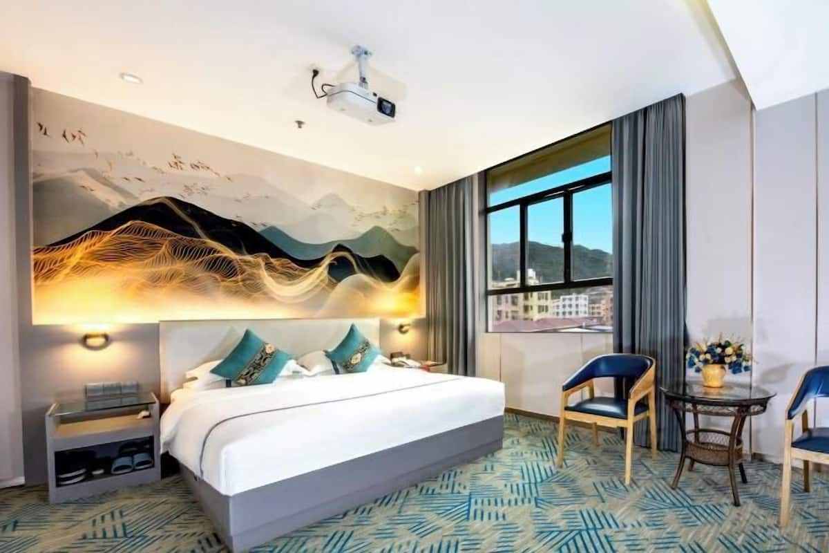 Ein Hotelzimmer mit einem großen Bett, einem Schreibtisch, zwei Stühlen, einem Fenster mit Blick und einem Projektor an der Decke.