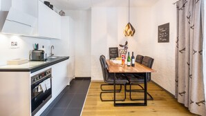 A compact kitchen with modern appliances, a dining area with a wooden table and chairs, and a decorative pendant light. - Apartment "Andy's Bergjuwel" with Mountain View, Wi-Fi & Balcony (Leutasch)