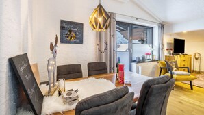 A modern living room with a dining table, grey chairs, a white furry rug, a decorative deer sculpture, a chandelier, and a window with curtains. - Apartment "Andy's Bergjuwel" with Mountain View, Wi-Fi & Balcony (Leutasch)