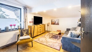 A modern living room with a large window, a flat-screen TV, a wooden cabinet, a sofa, and a coffee table. - Apartment "Andy's Bergjuwel" with Mountain View, Wi-Fi & Balcony (Leutasch)